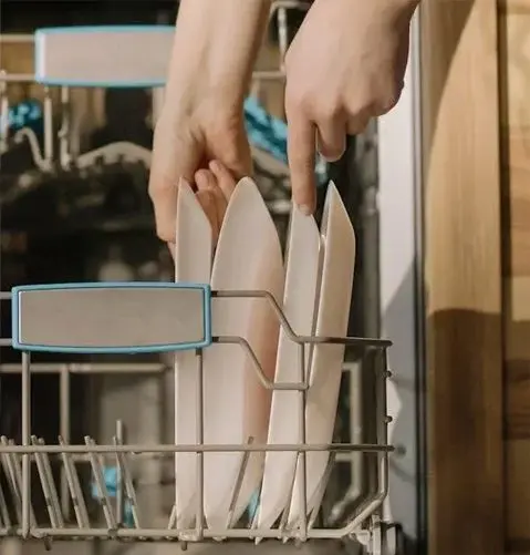 A person is loading some food into the dishwasher.